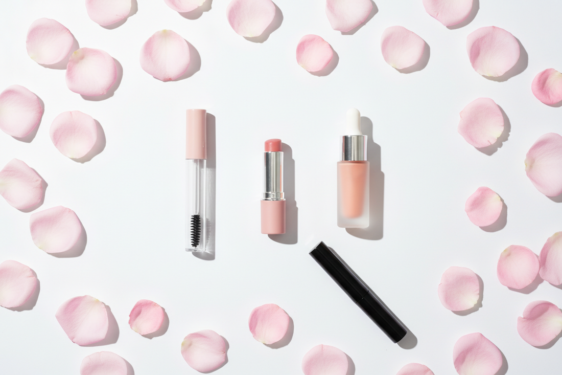 `Clean beauty flat lay with lip balm, liquid blush, mascara, and brow gel on white background with pink rose petals — non-toxic safe makeup guide for tweens and teens at BodyWell1.com`