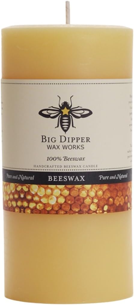 A large cylindrical beeswax candle in pale yellow wax with a white paper label reading 'Big Dipper Wax Works' and '100% Beeswax,' plus a honeycomb pattern near the bottom.