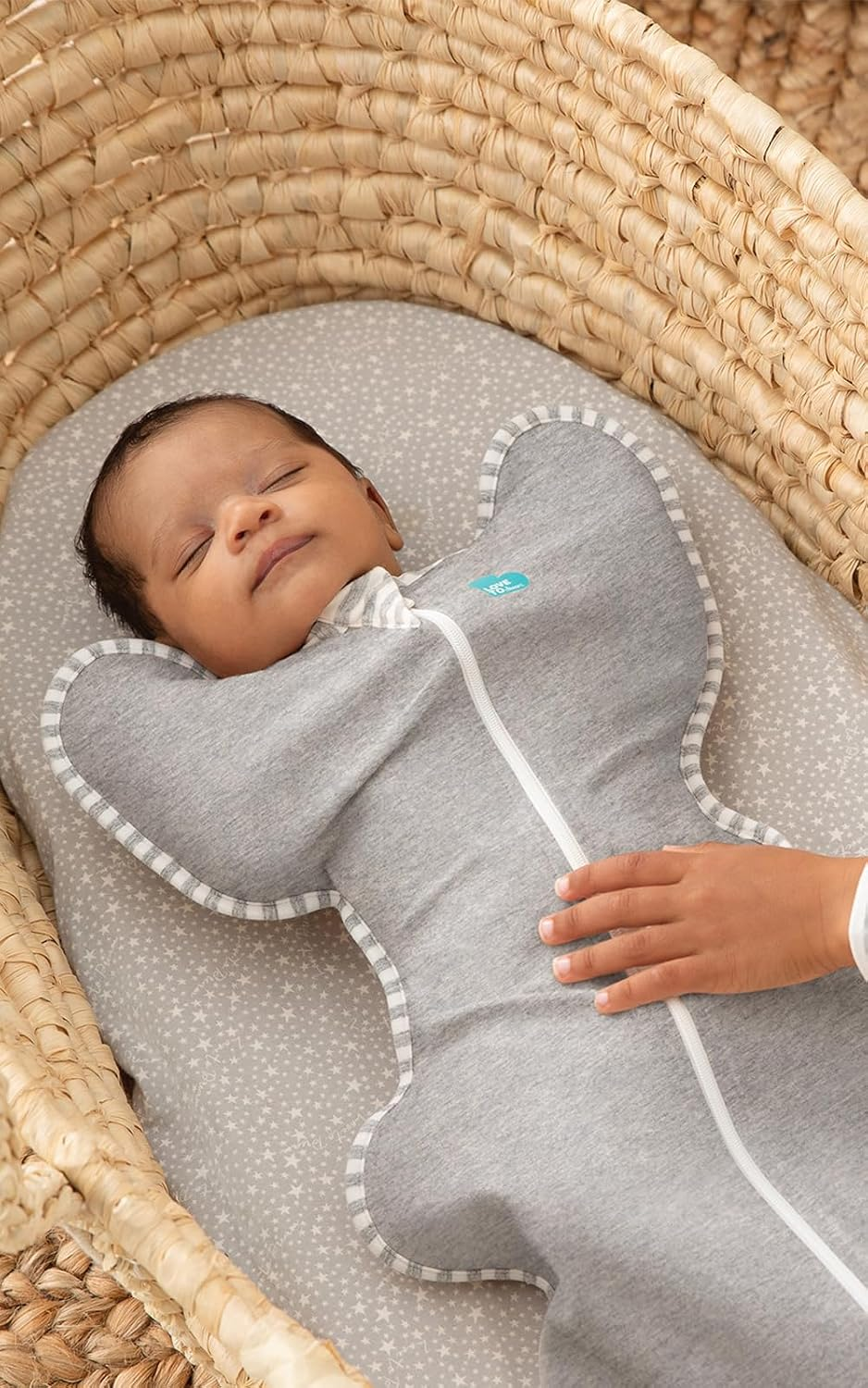 Newborn baby sleeping peacefully in Love to Dream Swaddle UP gray in a wicker bassinet — arms-up swaddle for safe natural sleep position