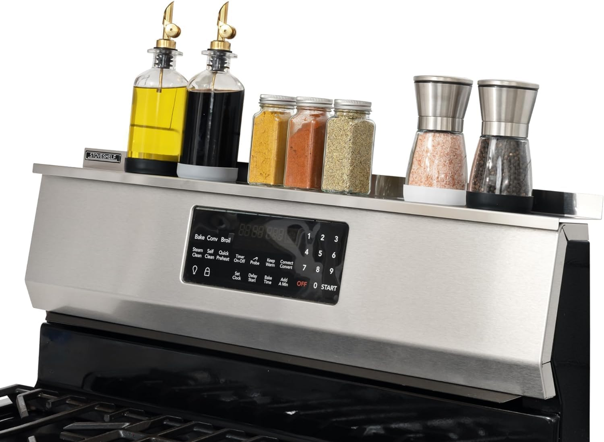 StoveShelf stainless steel finish magnetic shelf mounted above a stove control panel, shown holding bottles, spice jars and grinders.