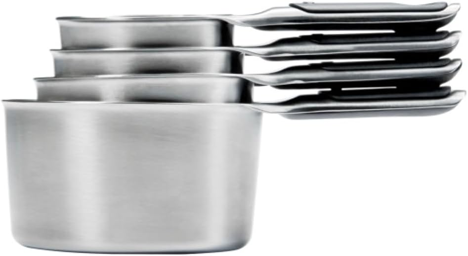 Four stainless steel dry measuring cups with magnetic handles, etched markings, and soft-grip handles on a white background.